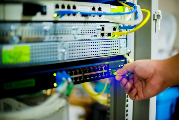 Hand holding fiber optic cord with Ethernet cables and network switching hub.